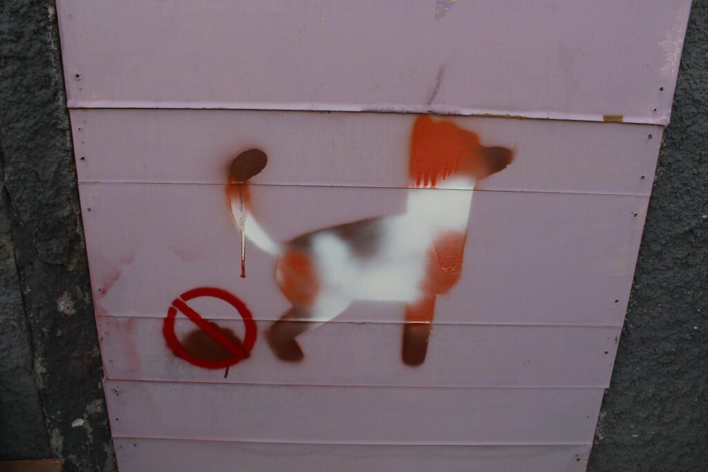 Grafiti de la silueta de un perro que ha hecho caca, la cual tiene el símbolo de prohibido sobre ella