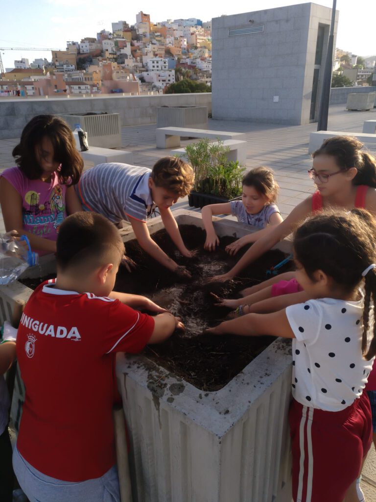 Niños y niñas plantando plantas en un macetero grande de hormigón