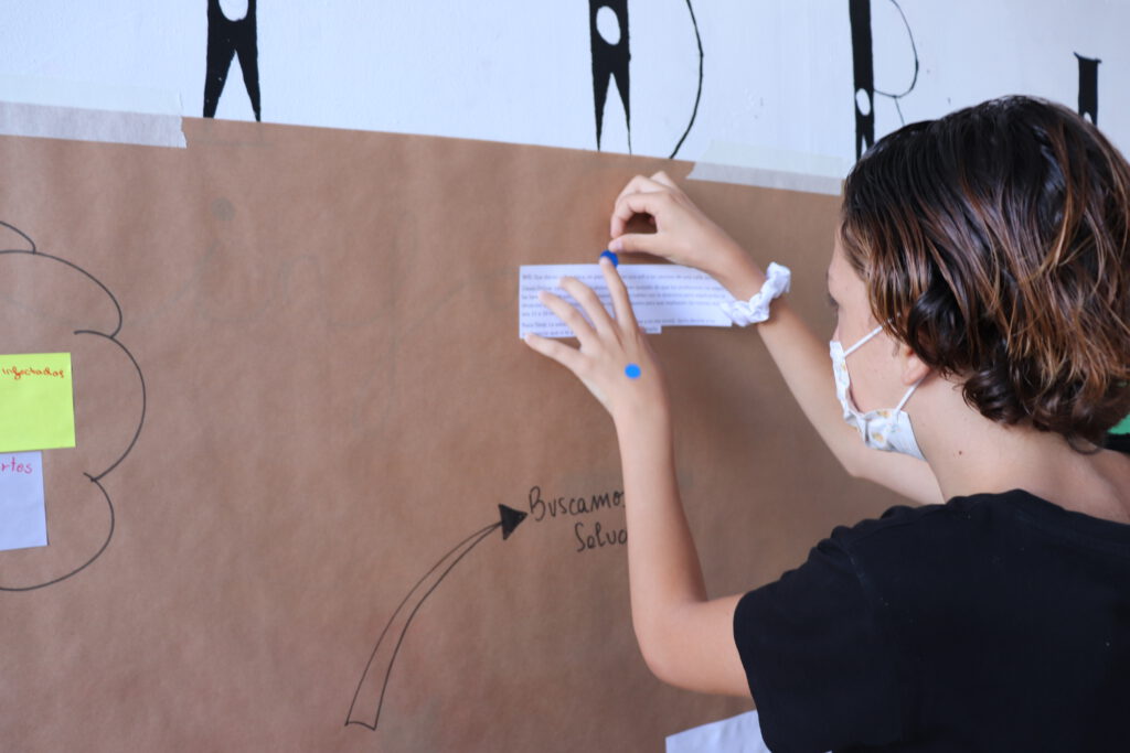 Un adolescentes pegando un papel escrito en un mural en la pared en el que hay escrito: buscamos soluciones